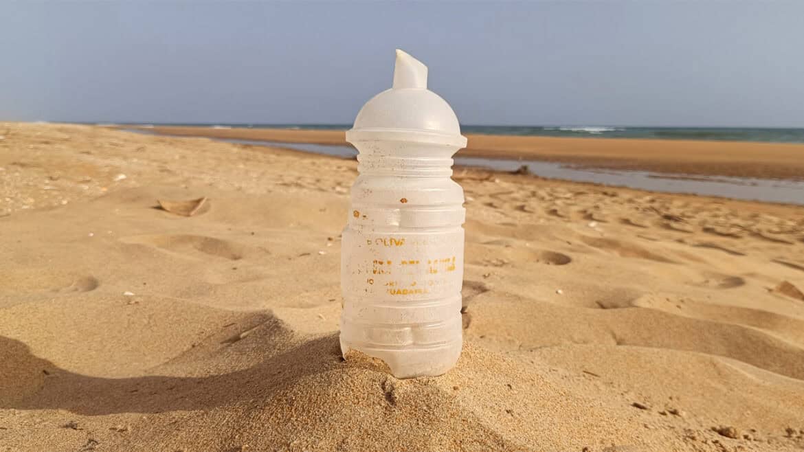 A Botella de aceite de oliva de los años 70 parcialmente enterrada en la arena destaca en la playa, con el mar y el cielo de fondo.