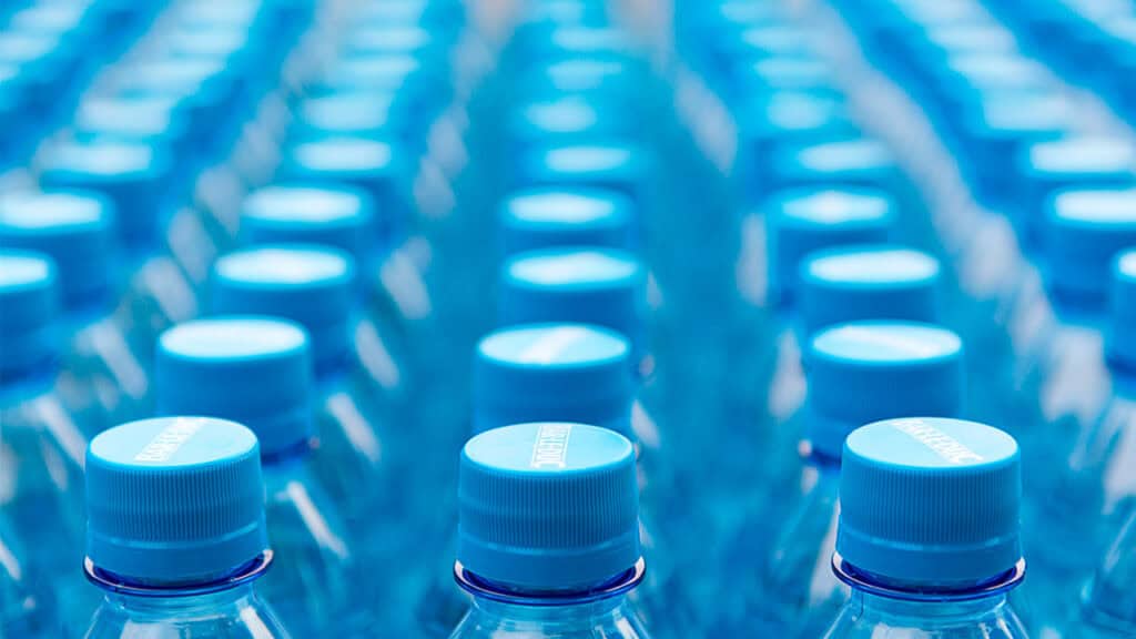 Filas de botellas de agua de plástico con tapones azules dispuestas muy juntas, creando un patrón repetitivo y poniendo de relieve el uso de plástico reciclado en envases alimentarios.