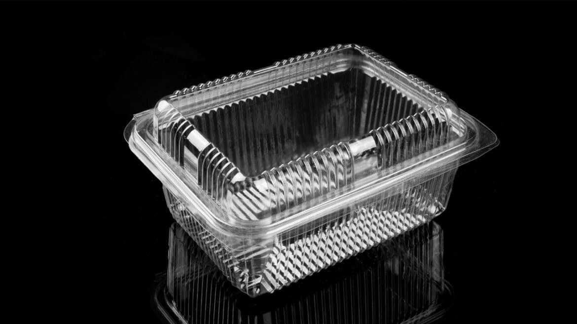 Recipiente de plástico transparente para comida para llevar con tapa abatible, fabricado con plástico reciclado procedente de envases alimentarios, vacío, expuesto sobre una superficie negra brillante.
