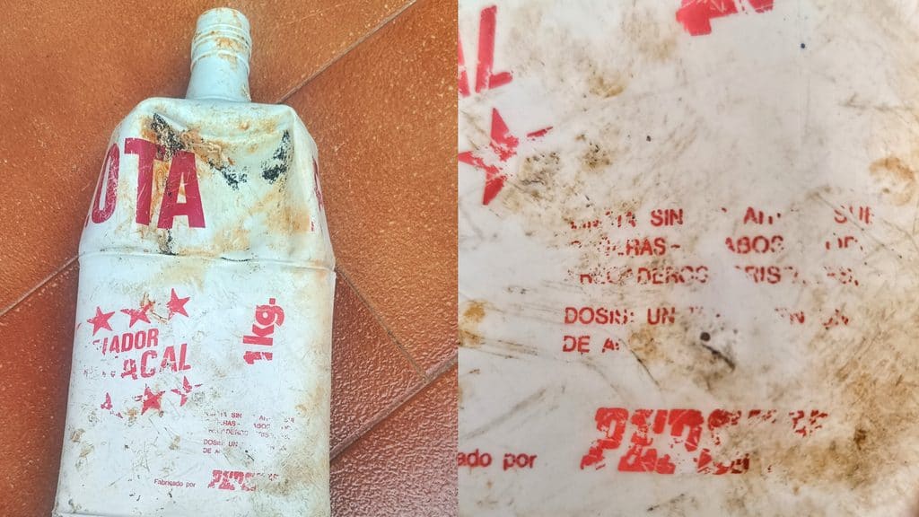 Un recipiente de plástico blanco, sucio y abollado, con la etiqueta «Limpiador Flota» y un texto rojo descolorido y estrellas, yace sobre un suelo de baldosas; un primer plano muestra unas instrucciones desgastadas e ilegibles que recuerdan a los productos de limpieza de los años 80.